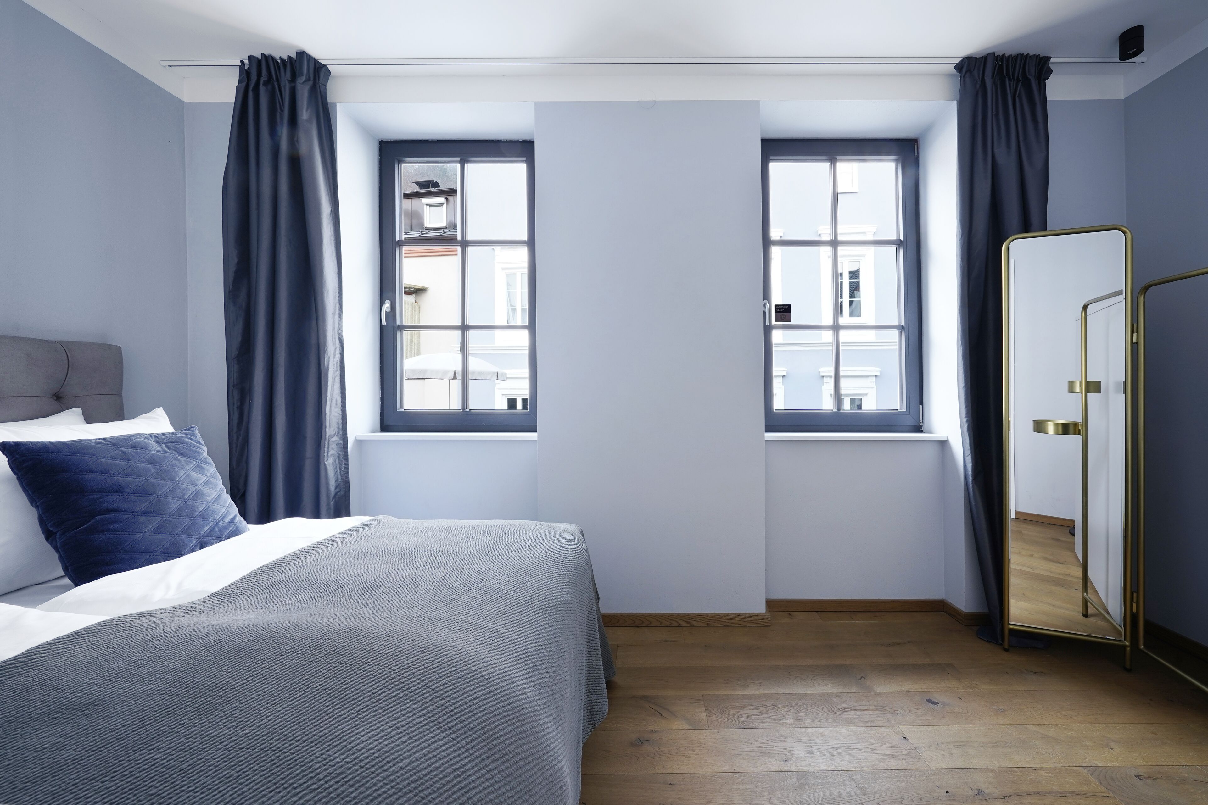 Une chambre à coucher avec un lit, deux fenêtres, un miroir et une armoire.