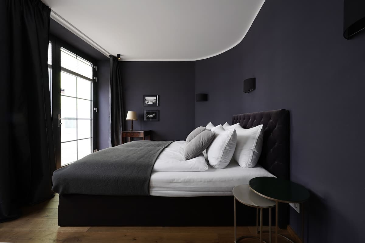 A modern bedroom with a large bed, dark walls, and a window with curtains.