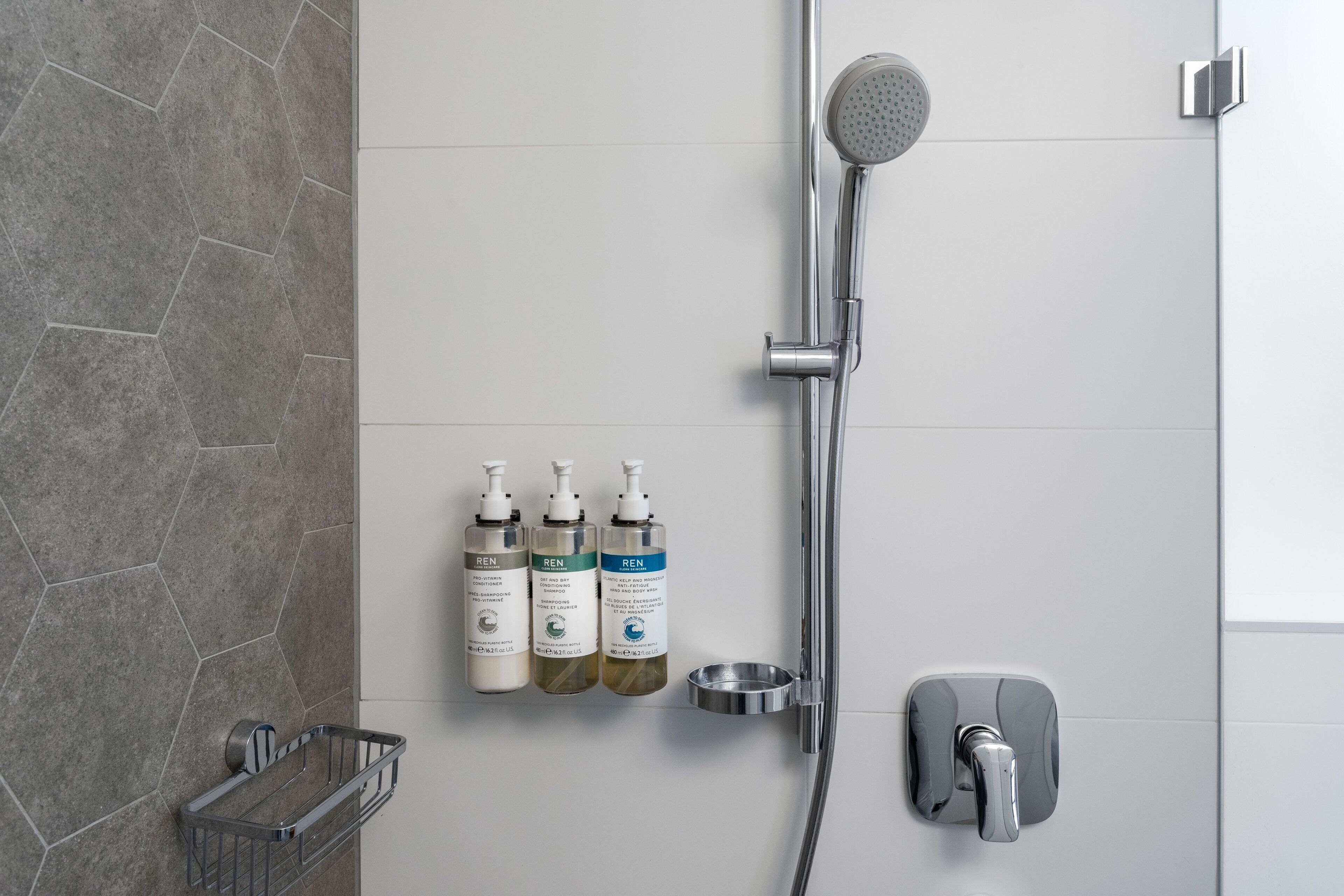 A modern bathroom with a shower, three toiletry bottles, and a soap dish.