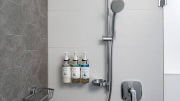 A modern bathroom with a shower, three toiletry bottles, and a soap dish.