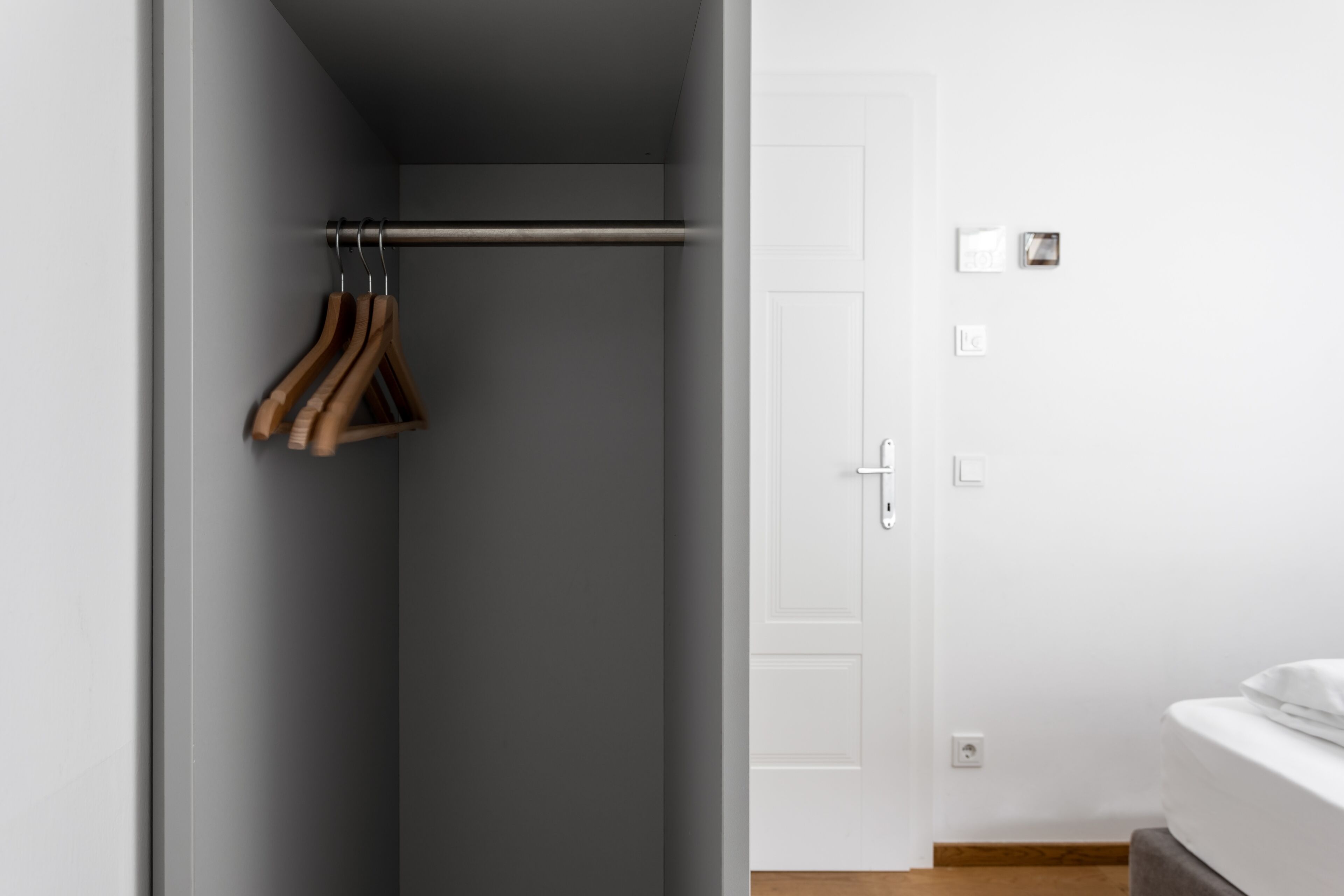 A room with a grey wall, a white door, and a bed with white bedding.