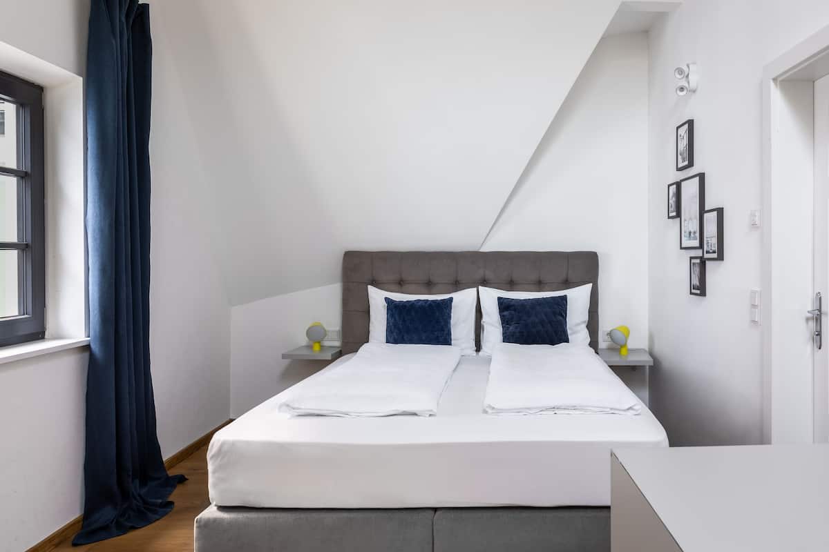 A neatly made bed with white linens, a grey upholstered headboard, and two bedside tables with lamps.