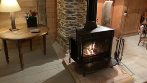 A cozy room with a stone wall, a wooden table with a lamp, and a wood-burning stove.
