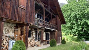 A rustic wooden building with a stone foundation, a balcony with a lattice railing, and a well-maintained garden with trimmed bushes and a lawn.