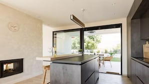 Une cuisine moderne dotée d’un grand îlot central, d’un four encastré et d’un coin repas offrant une vue sur l’extérieur.