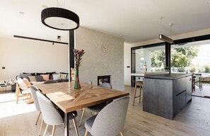 Una cocina moderna con una isla central, un comedor con mesa y sillas de madera, y una sala de estar con sofá y chimenea.