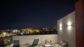 Une terrasse sur le toit offrant une vue sur la ville, dotée d’une balustrade en verre et d’un espace détente avec une table et des chaises.