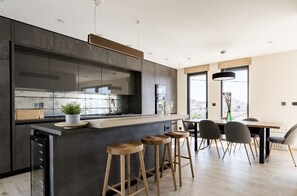 Una cocina moderna con una isla central, taburetes de bar y un comedor con sillas.