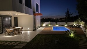Une maison moderne dotée d’une piscine, d’un espace salon extérieur et d’un patio bien éclairé.