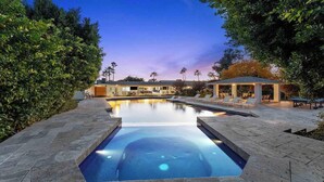 A swimming pool with a modern design, surrounded by a landscaped garden and a covered patio area. - 7BR Luxury Retreat - Cedar Sauna, Gym, Heated Pool, Spa, Basketball & Foosball (Scottsdale)