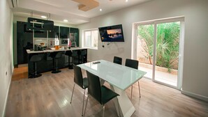 Una cocina moderna con armarios oscuros, una encimera blanca y una zona de comedor con una mesa de vidrio y sillas negras.