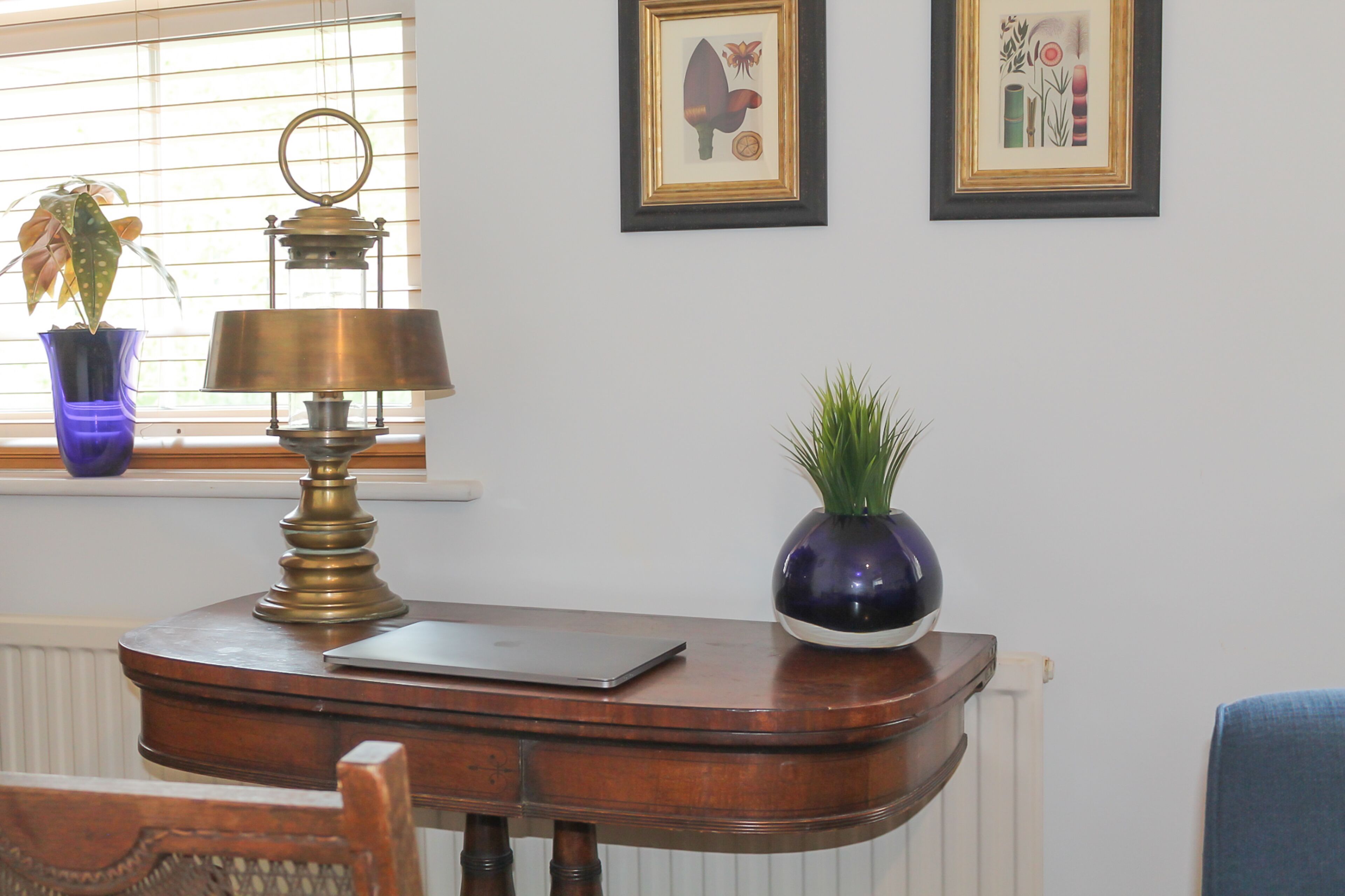 Una scrivania in legno con una lampada in ottone, un computer portatile e una pianta in vaso.