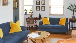 A living room with a blue sofa, yellow cushions, a wooden coffee table, and a leather armchair. - Sydney Wharf House (Bath)