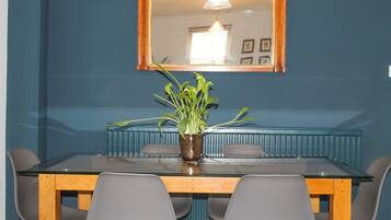 Een eetgedeelte met een tafel met glazen blad, vier grijze stoelen, een houten bank en een pot met plant.