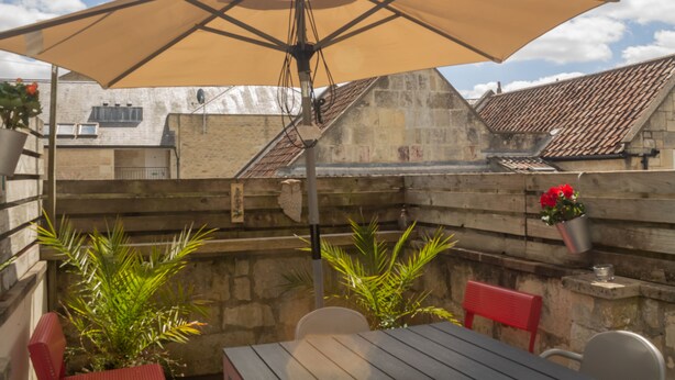 An outdoor patio with a table and chairs, a large umbrella, and potted plants. - Sydney Wharf House (Bath)