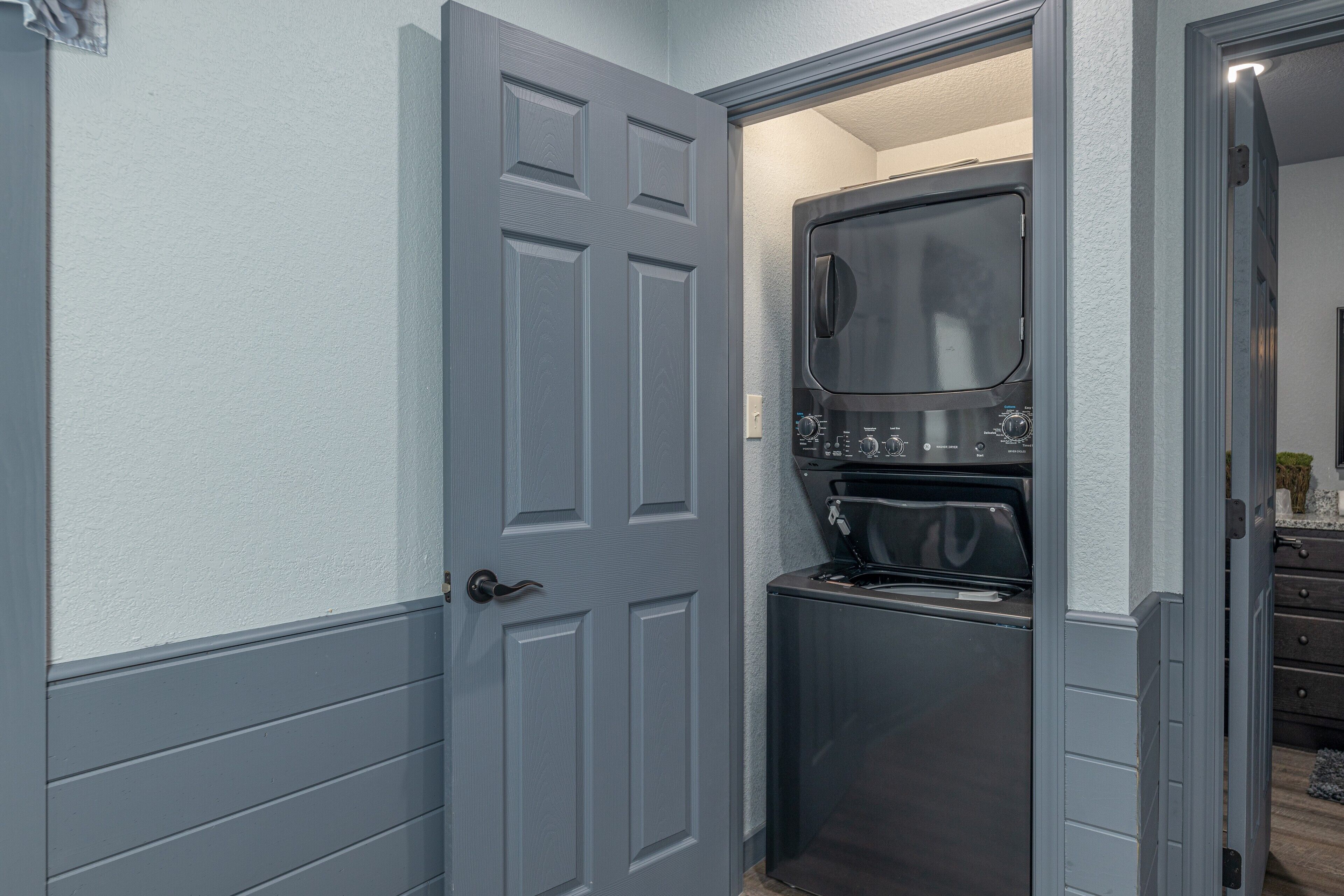 A compact laundry room with a built-in washer and dryer, a gray door, and a small countertop.
