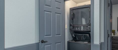 A compact laundry room with a built-in washer and dryer, a gray door, and a small countertop.