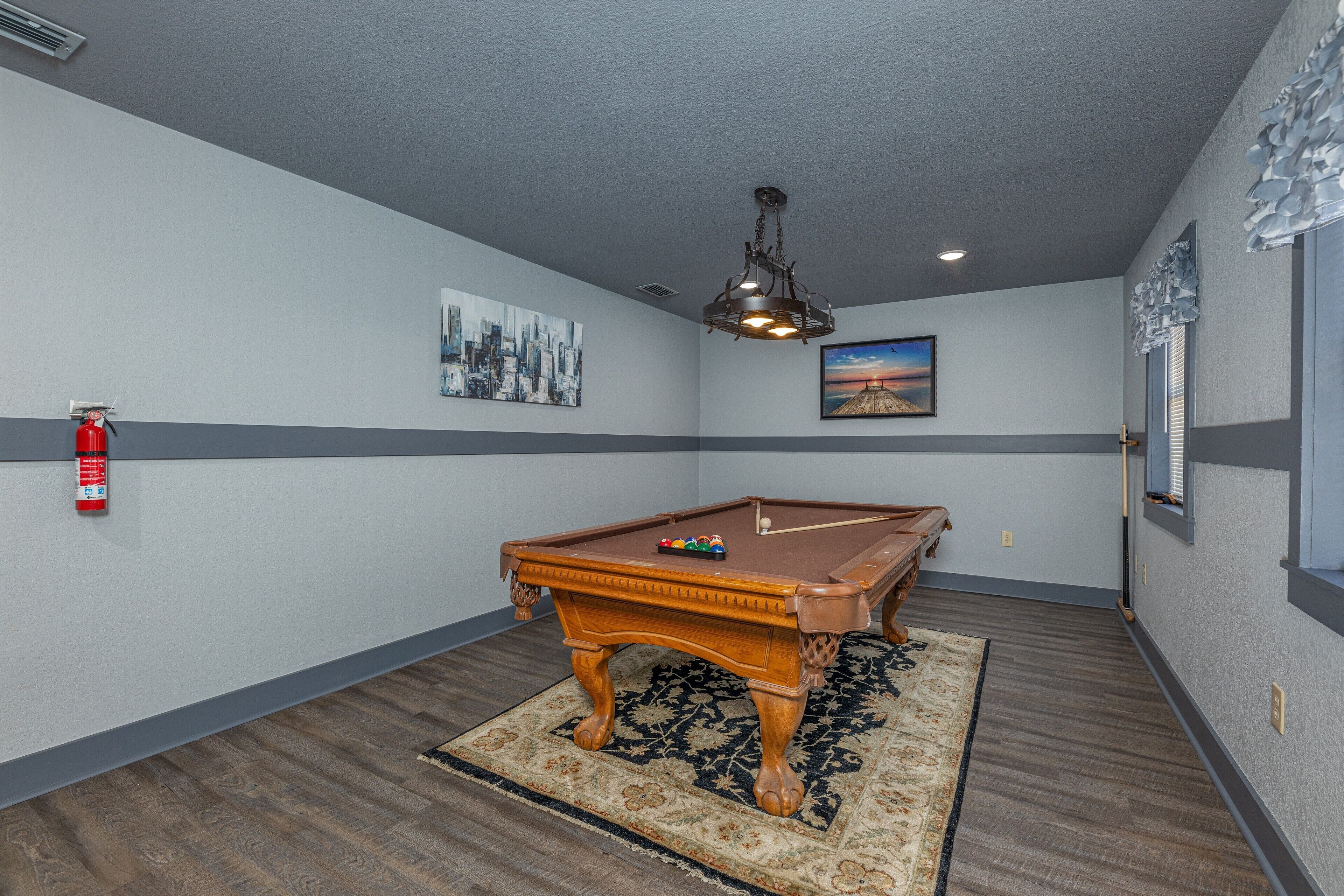 A pool table in a room with gray walls, a fire extinguisher, and a ceiling light fixture.