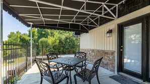 Une terrasse extérieure avec une table et des chaises, un espace abrité, un mur en pierre et une porte avec une fenêtre.