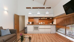 Une cuisine moderne avec des meubles en bois, un four encastré et un four à micro-ondes. On y trouve également un coin repas avec une table en verre et un canapé.