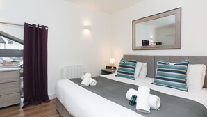 Une chambre d’hôtel avec un grand lit, une table de chevet avec une lampe, un miroir et une fenêtre avec des rideaux.