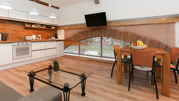 Une cuisine moderne avec des meubles en bois, un coin repas comprenant une table et des chaises, et une grande fenêtre avec des stores.