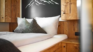 Una cama bien hecha con ropa blanca y dos almohadas, cabecero de madera y un interruptor de luz en la pared.
