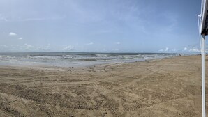 Een zandstrand met zachte golven, een heldere lucht en gebouwen in de verte.