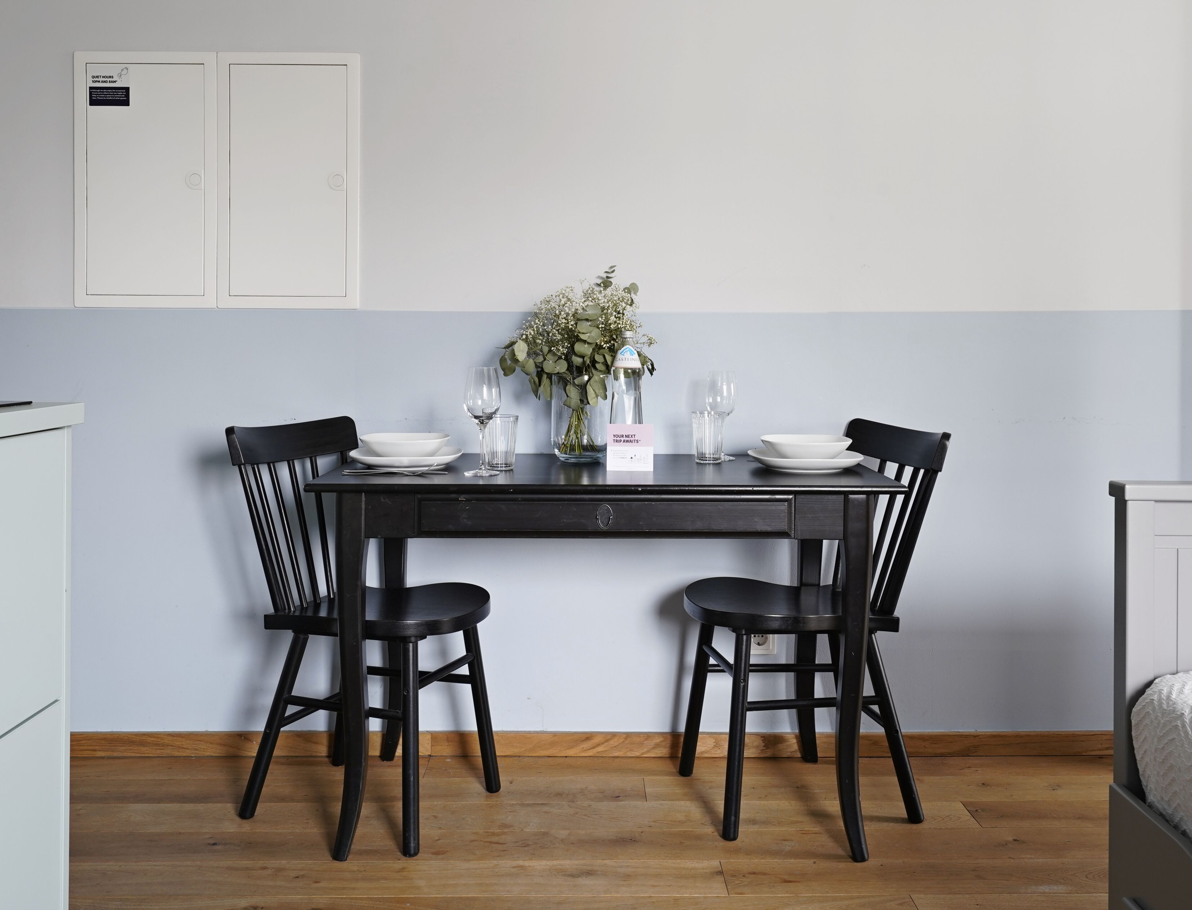 A dining table with two black chairs, a vase with flowers, and a sign on the wall.