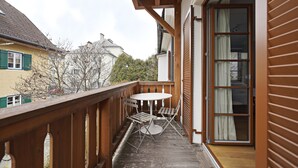 Ein Holzbalkon mit Tisch und Stühlen, eine Schiebeglastür und Blick auf benachbarte Häuser.