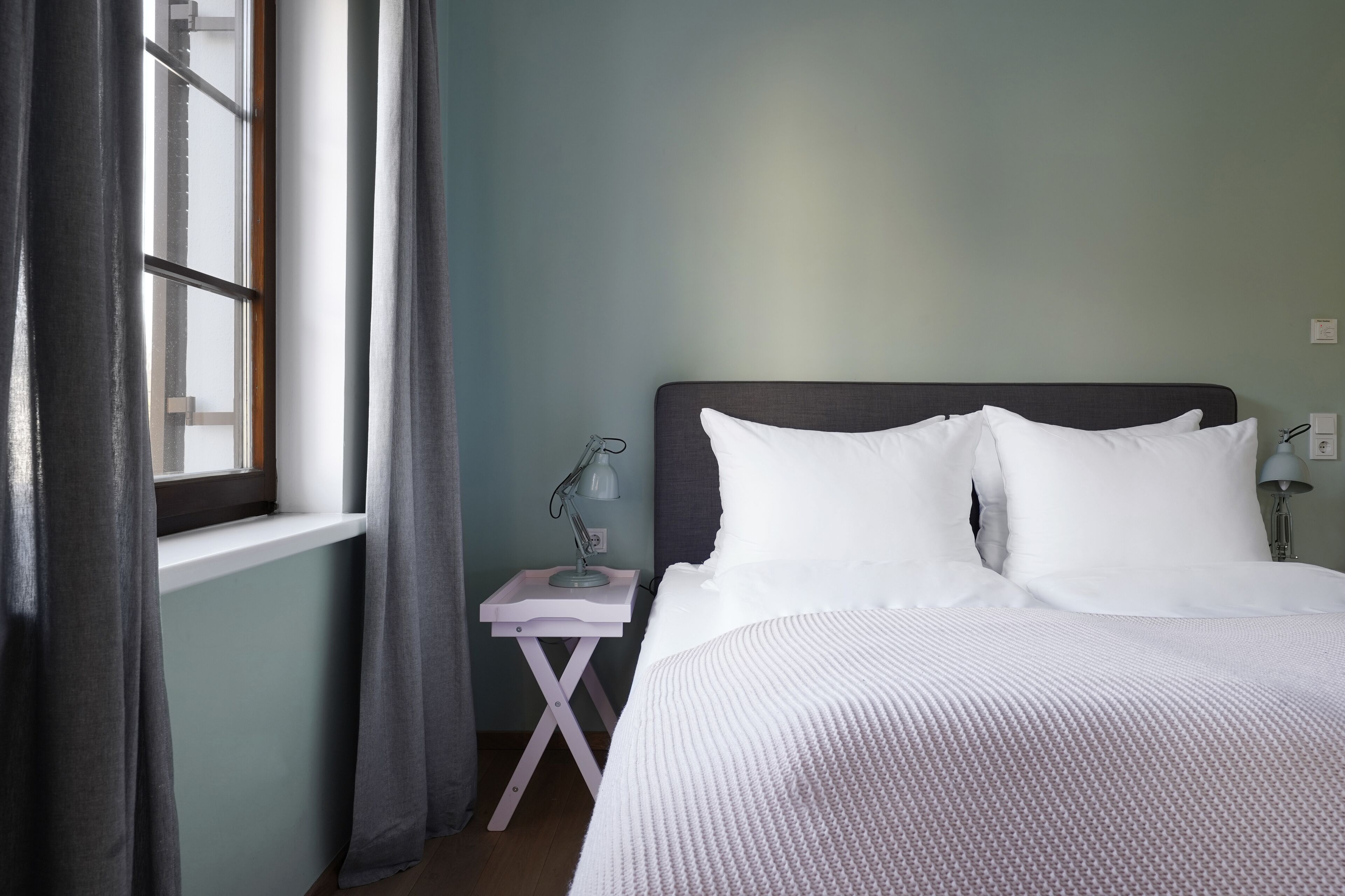 Una cama bien hecha con ropa blanca en una habitación con paredes verde claro.