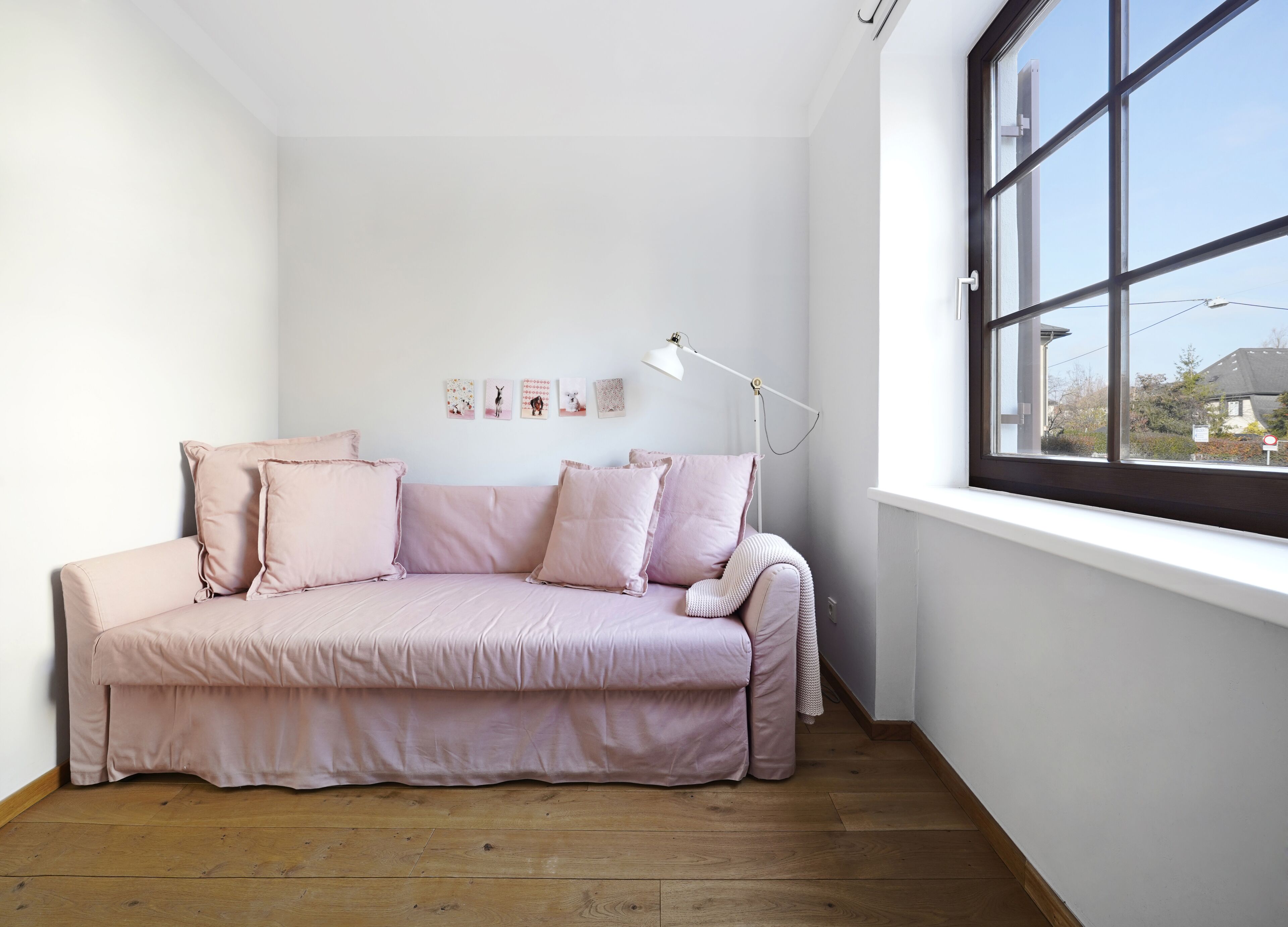 A minimalist room with a pink sofa, a white floor lamp, and a large window with a view of buildings.