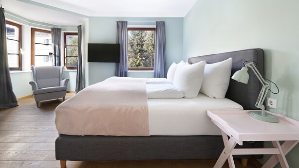 Ein Schlafzimmer mit Bett, Nachttisch, Lampe, Stuhl und Fernseher an der Wand.