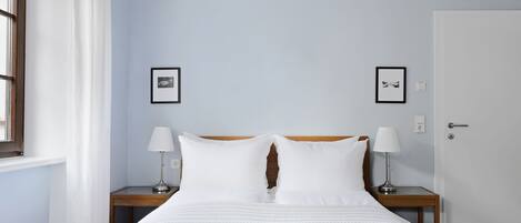 A neatly made bed with white linens, two bedside tables with lamps, and two framed pictures on the wall.