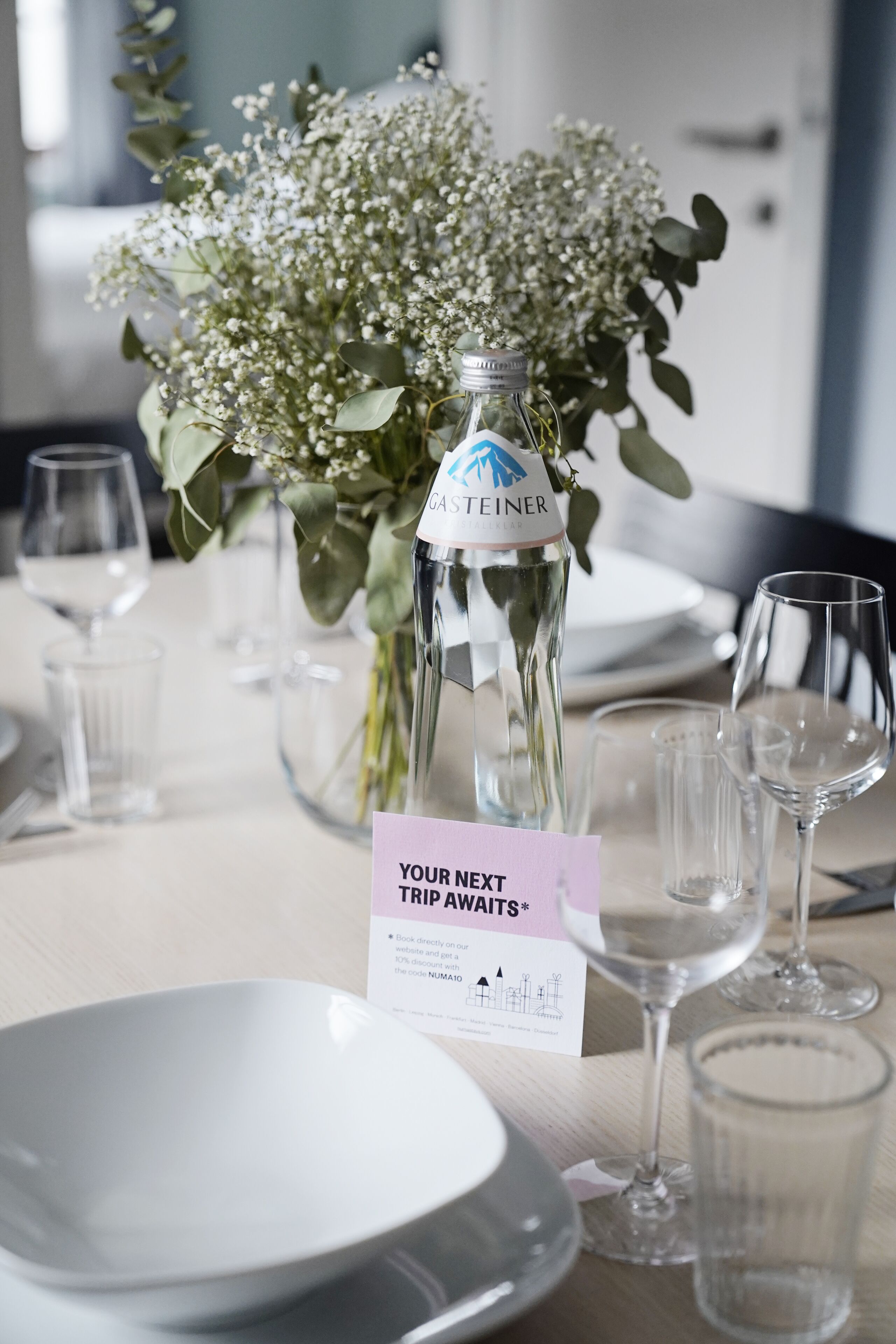 A table set with a bottle of champagne, a vase of flowers, and a sign indicating a trip awaits.