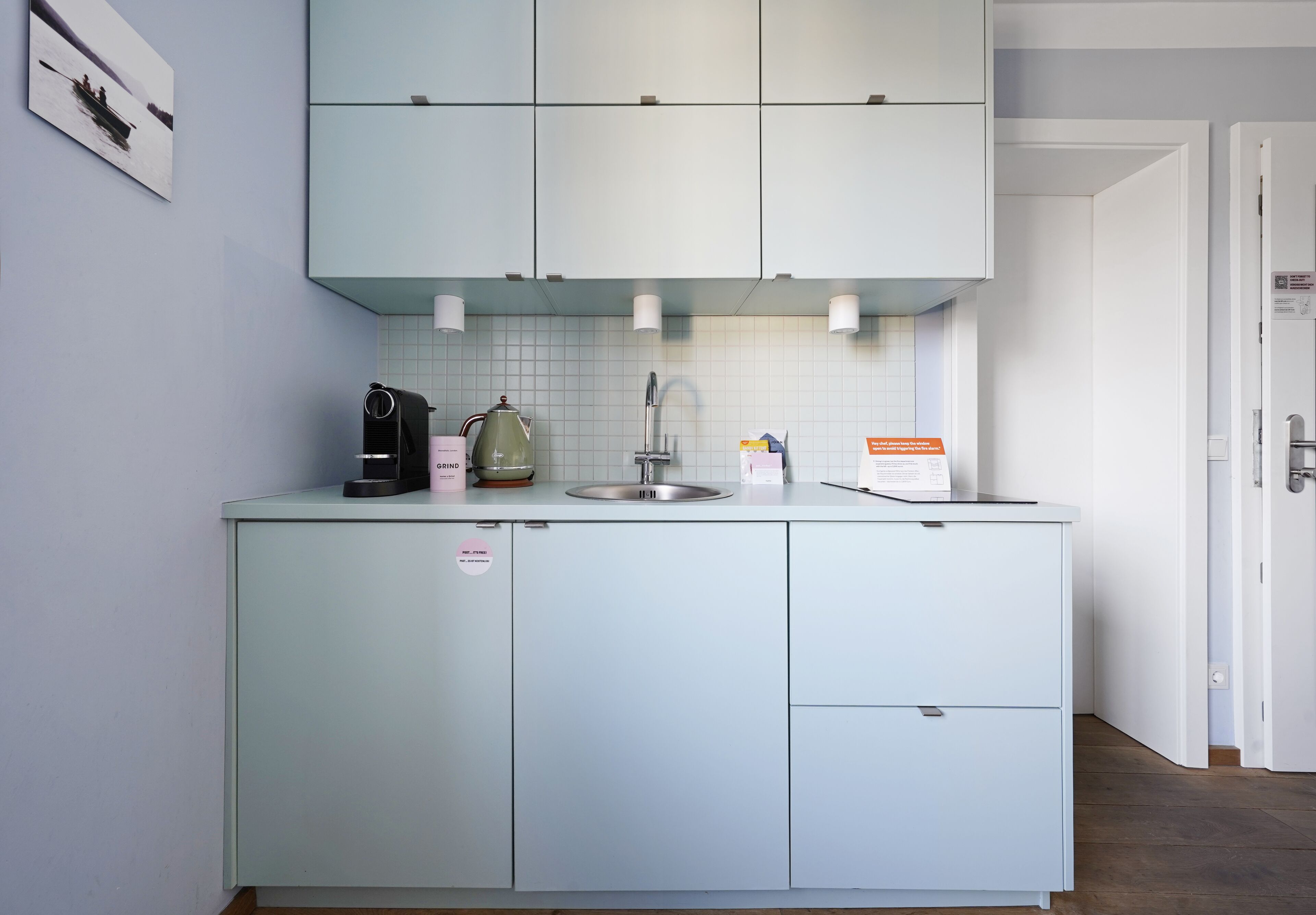 A kitchen with light blue cabinets, a coffee maker, a kettle, and a sink.
