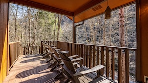 A wooden deck with chairs and a railing overlooking a forested area. - Southern Luxury (Sevierville)