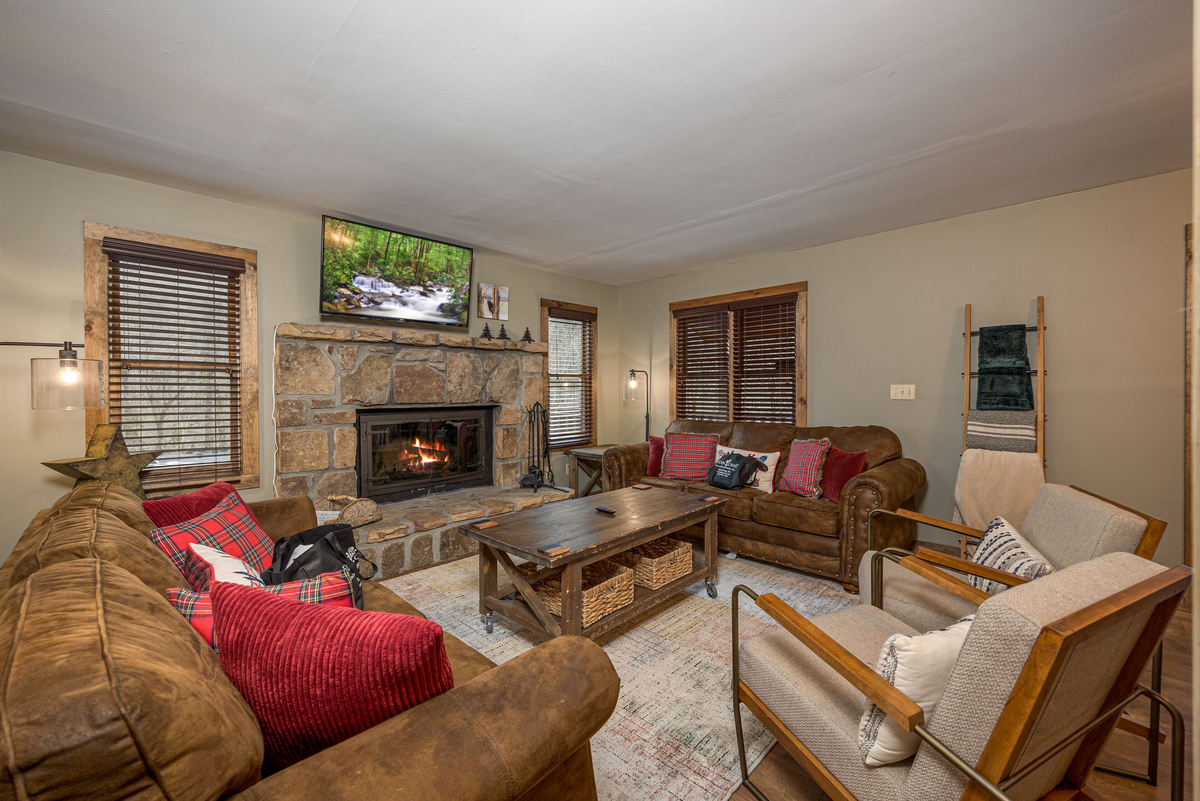 A cozy living room with a stone fireplace, comfortable seating, and a television mounted above the fireplace.