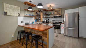 A modern kitchen with a central island, bar stools, stainless steel appliances, and wooden accents. - Southern Luxury (Sevierville)