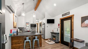 Una cocina moderna con una isla central, taburetes de bar, una chimenea y un televisor en la pared.