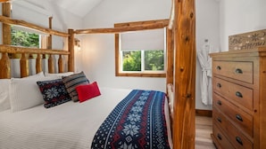 Un dormitorio con techo de madera, cama con ropa de cama estampada, cómoda y ventana con vista a zonas verdes.