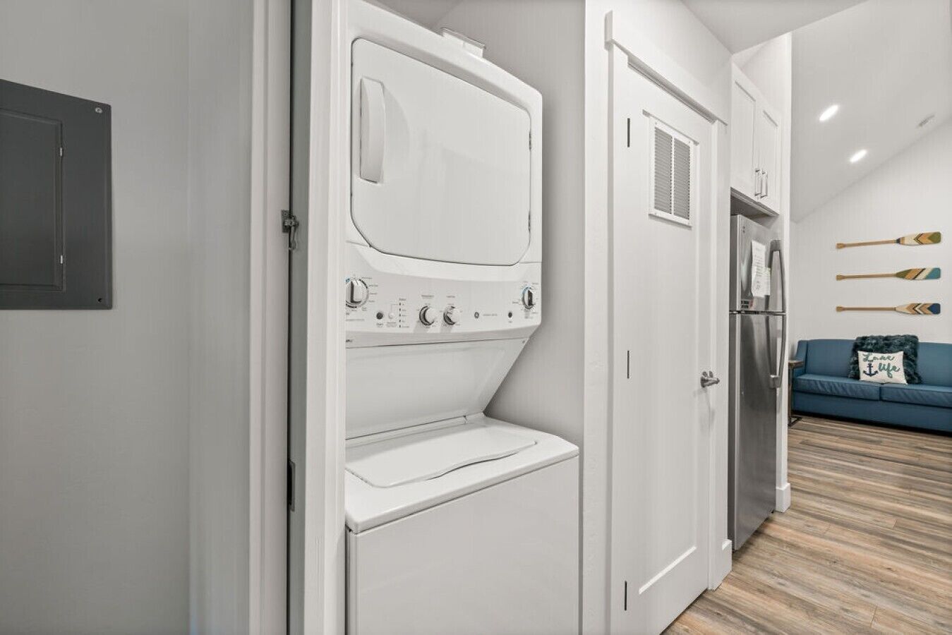 A compact laundry room with a washer and dryer, a small seating area with a blue sofa, and a wall-mounted rack with paddles.