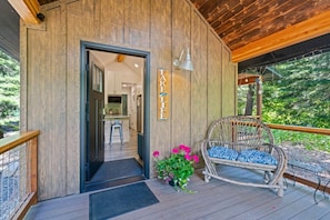 A wooden exterior with a door leading to an interior kitchen area, a wicker chair, and a small potted plant with pink flowers.