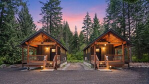 Two wooden cabins with a gravel driveway, surrounded by dense forest.