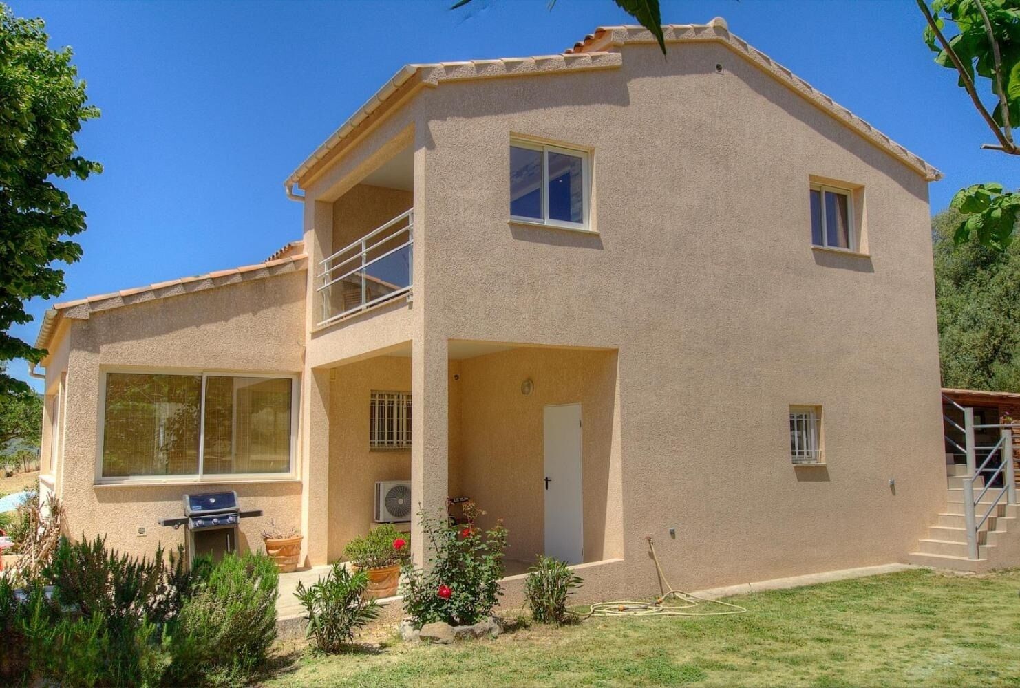 Une maison à deux étages avec un balcon, de grandes fenêtres et un petit jardin.