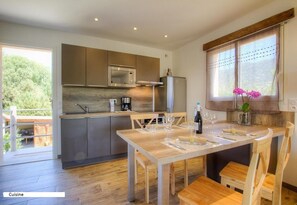 Une cuisine moderne équipée d’appareils électroménagers en acier inoxydable, une table à manger en bois pour quatre personnes et une vue sur l’extérieur.