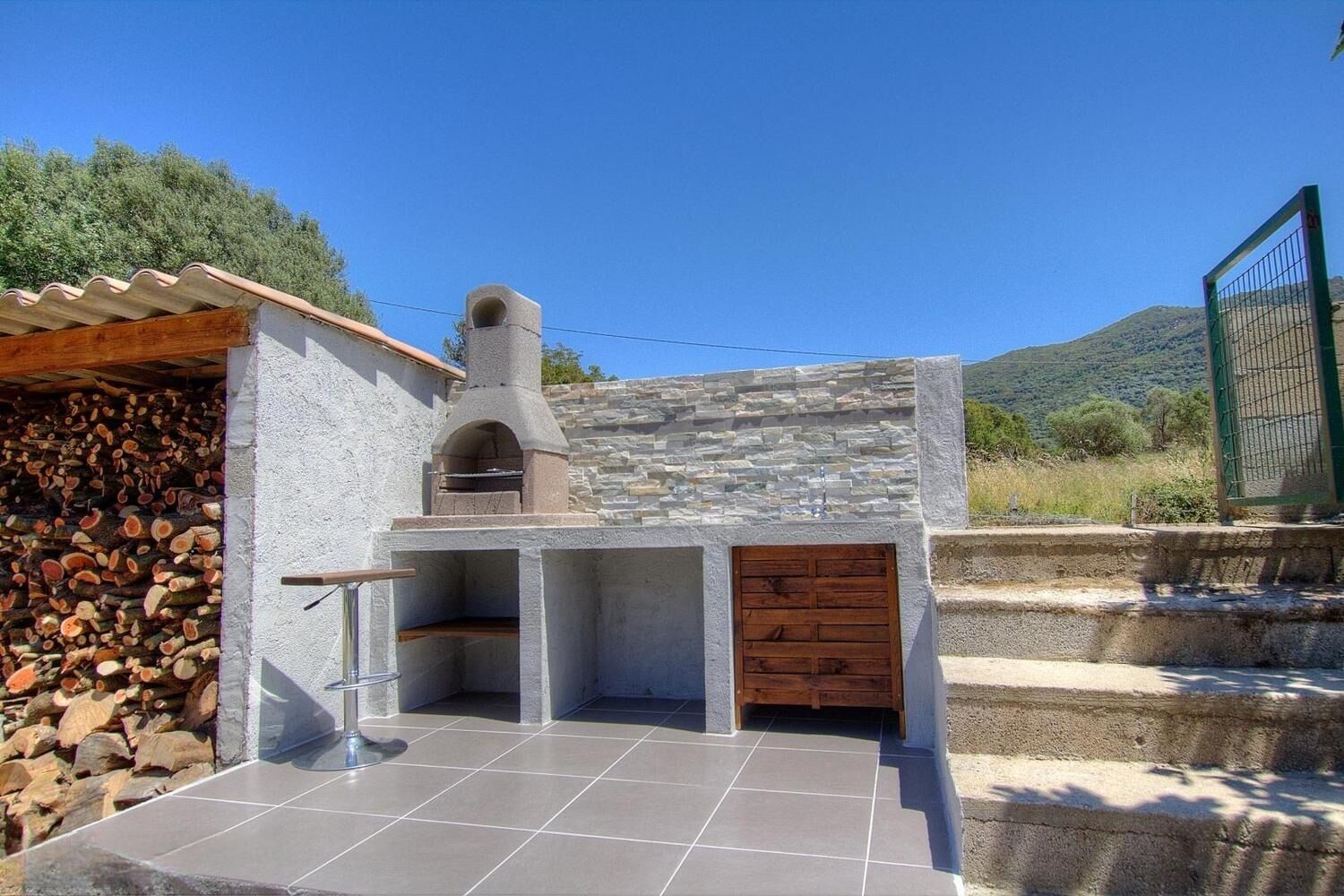 A stone-built outdoor kitchen with a chimney, a tiled patio, and a wooden door.