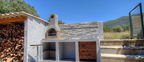 A stone-built outdoor kitchen with a chimney, a tiled patio, and a wooden door.