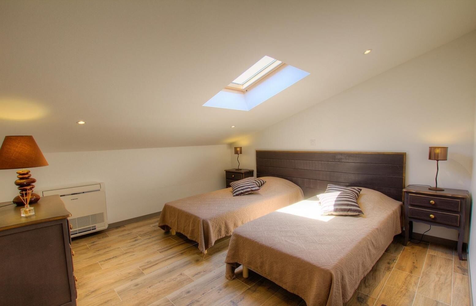 A bedroom with two beds, a skylight, a heater, and bedside lamps.