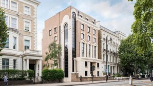 A multi-story building with a prominent central glass facade, a classical architectural style, and a well-maintained sidewalk. - Elegant 3BD Apartment in Earls Court (London)